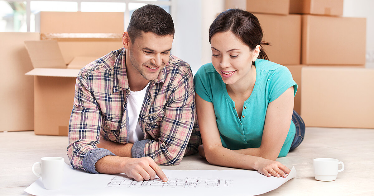 Young couple laying on floor while packing reviewing the plans of their new home