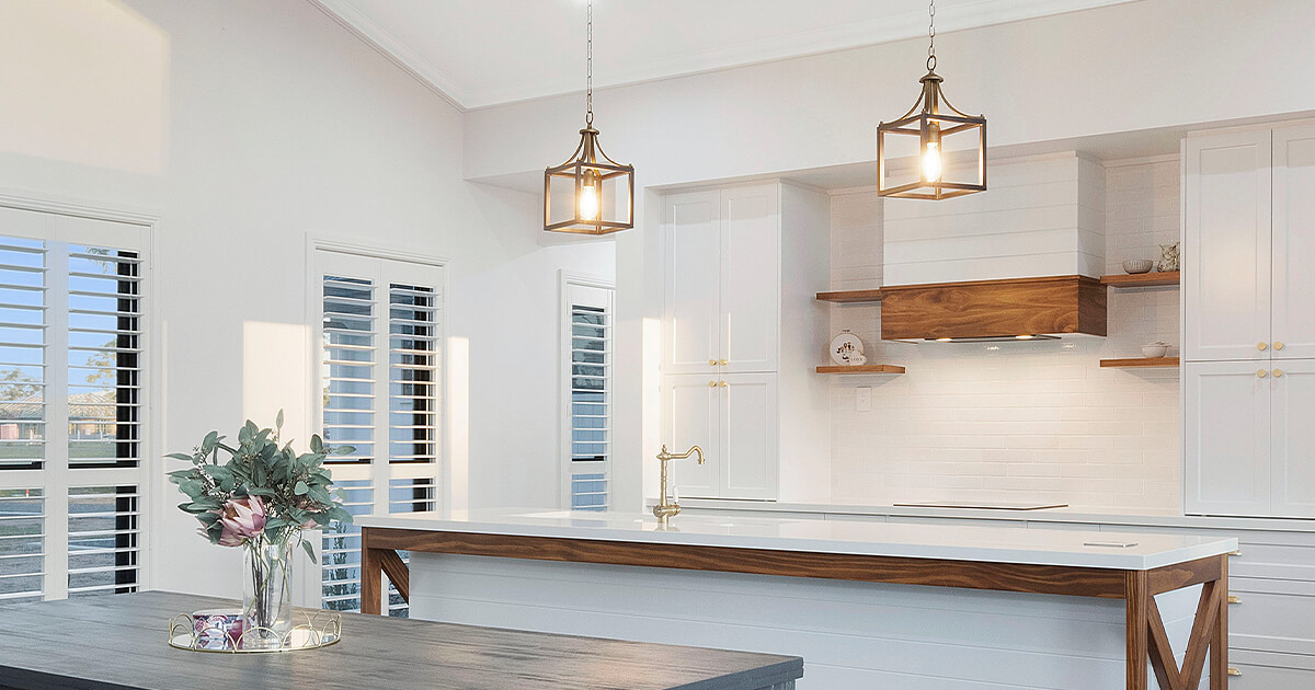 Well lit pendant lights hang above bright and white kitchen with timber accents