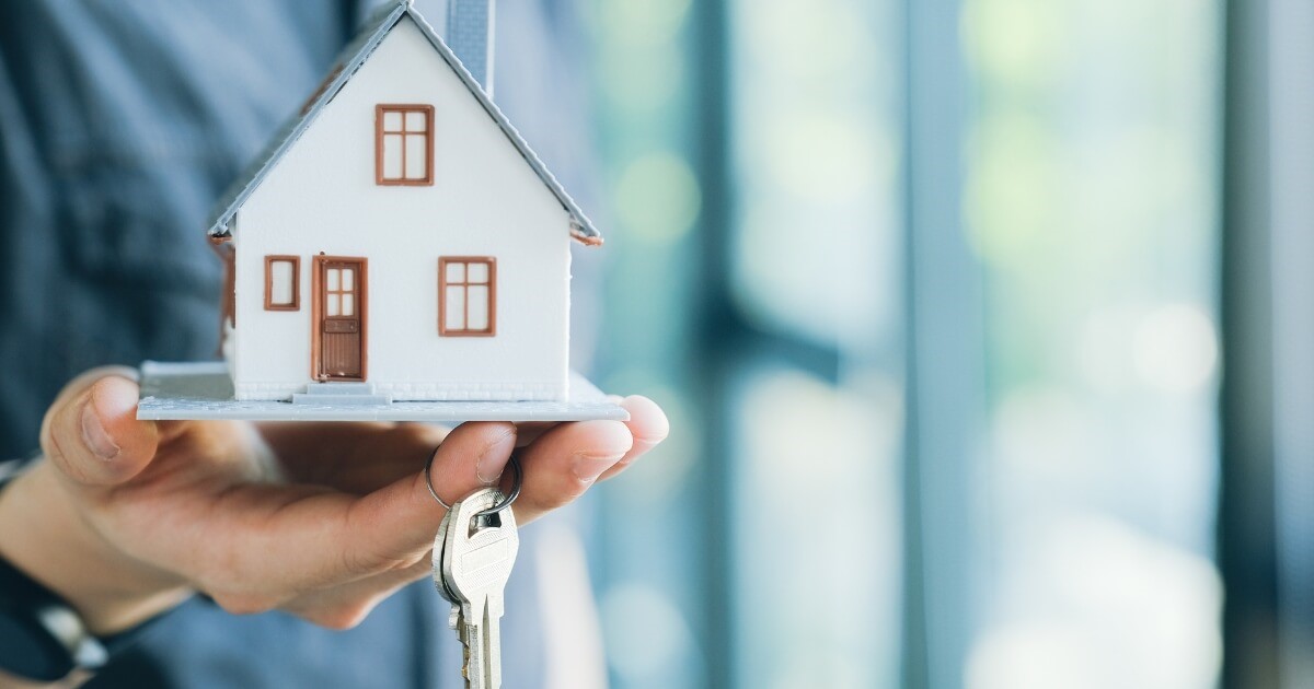 Mini house with a key in hands wondering whether to buy or build